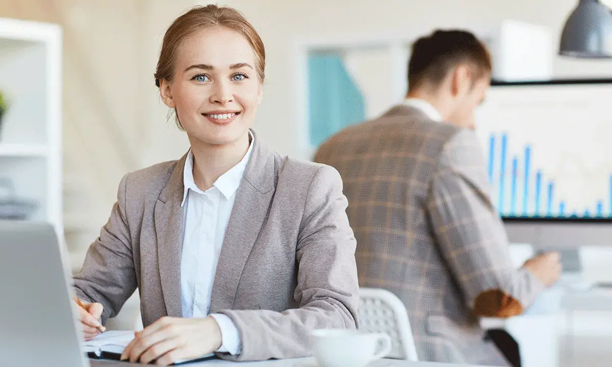 Mujer sonríe mientras se prepara para una entrevista de trabajo, tomando notas en su portátil.