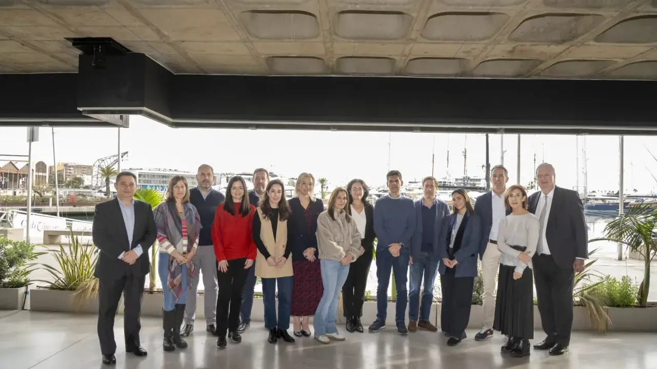 Grupo diverso posa para foto de graduación de un **advanced management program** frente a un puerto deportivo.