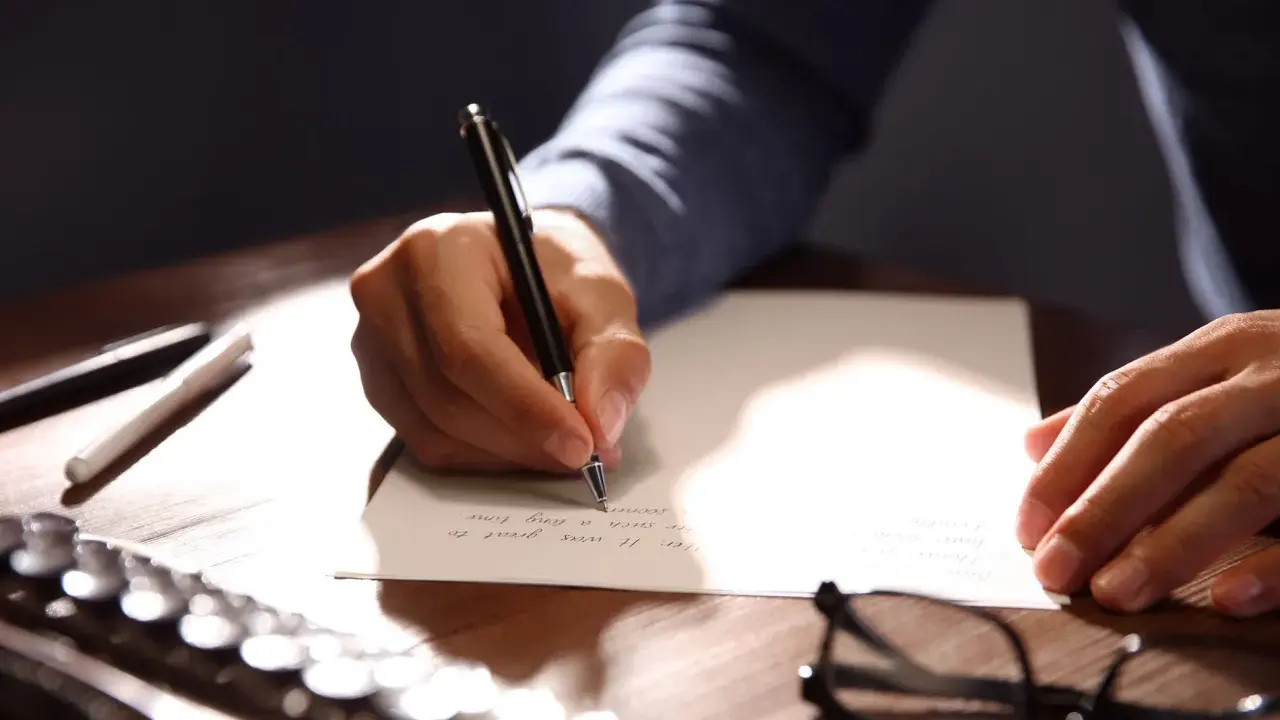 Mano escribiendo una carta formal con bolígrafo.