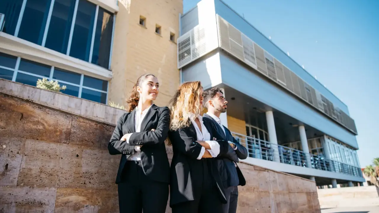 Tres jóvenes profesionales con trajes oscuros, con los brazos cruzados, posan frente a un edificio moderno. Aspiran a estar en los FT MBA rankings.