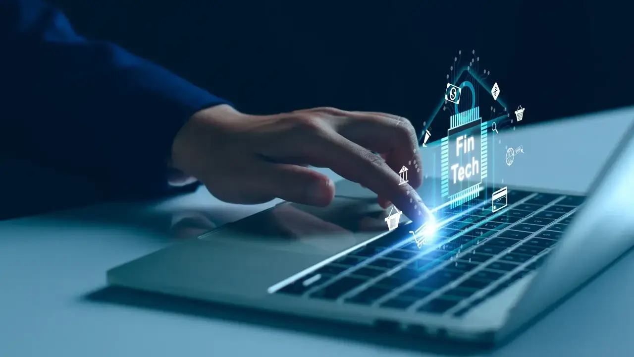 Dedo sobre teclado de laptop interactuando con un chip digital que muestra "Fin Tech" y varios iconos financieros, simbolizando el desarrollo de software fintech.