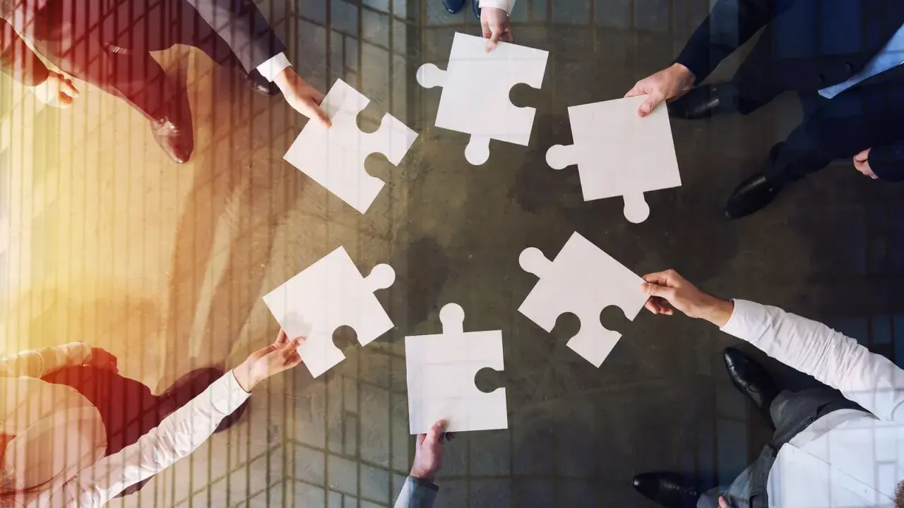 Manos unidas colocando piezas de rompecabezas, un símbolo de inteligencia colaborativa y trabajo en equipo para lograr un objetivo común.