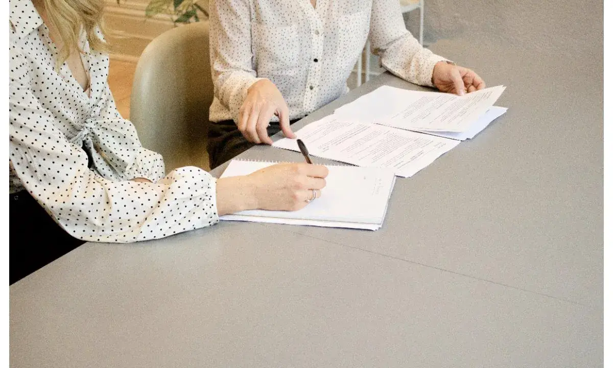 Dos mujeres revisan documentos en una mesa. Una escribe notas, un paso clave en cómo ser un CEO.