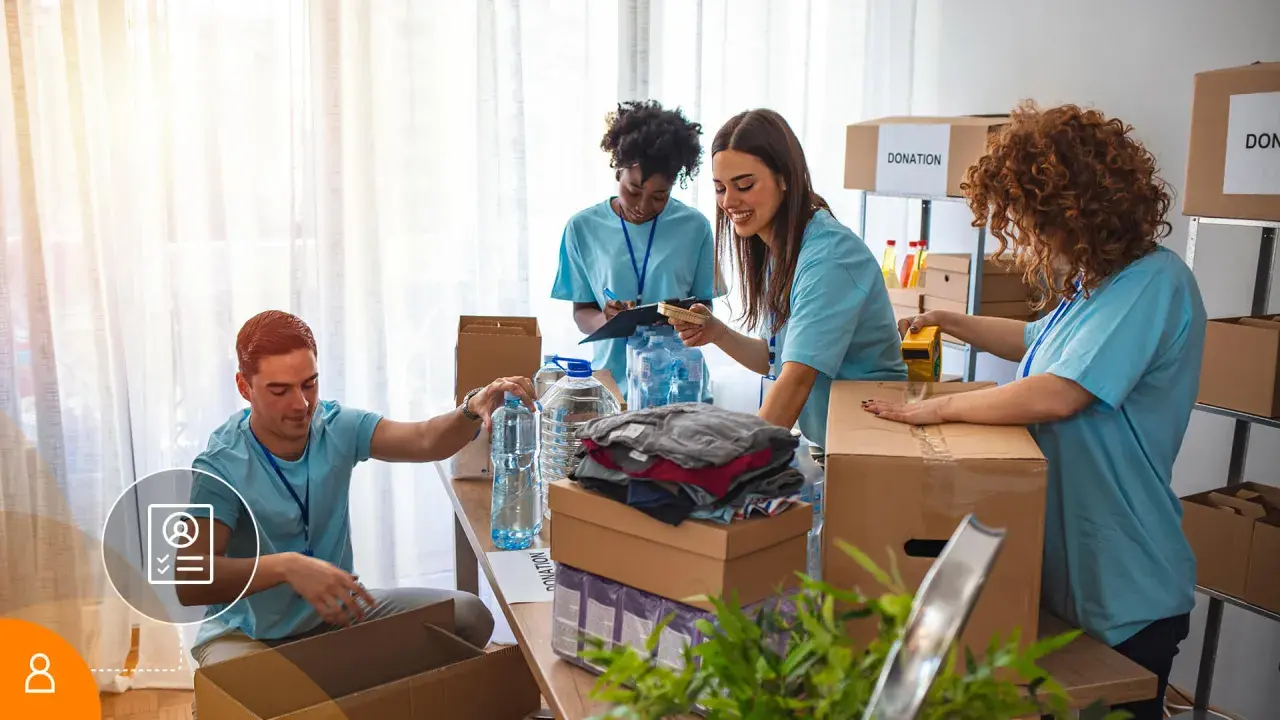 Voluntarios organizan donaciones. Un hombre revisa una lista, mientras otros empaquetan ropa y agua. Su cv volunteering es valioso.