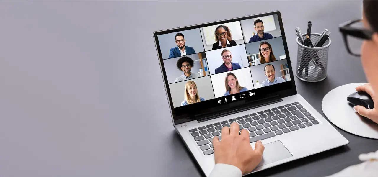 Persona interactúa con tecnología de videoconferencia, mostrando una cuadrícula de participantes en una reunión virtual.