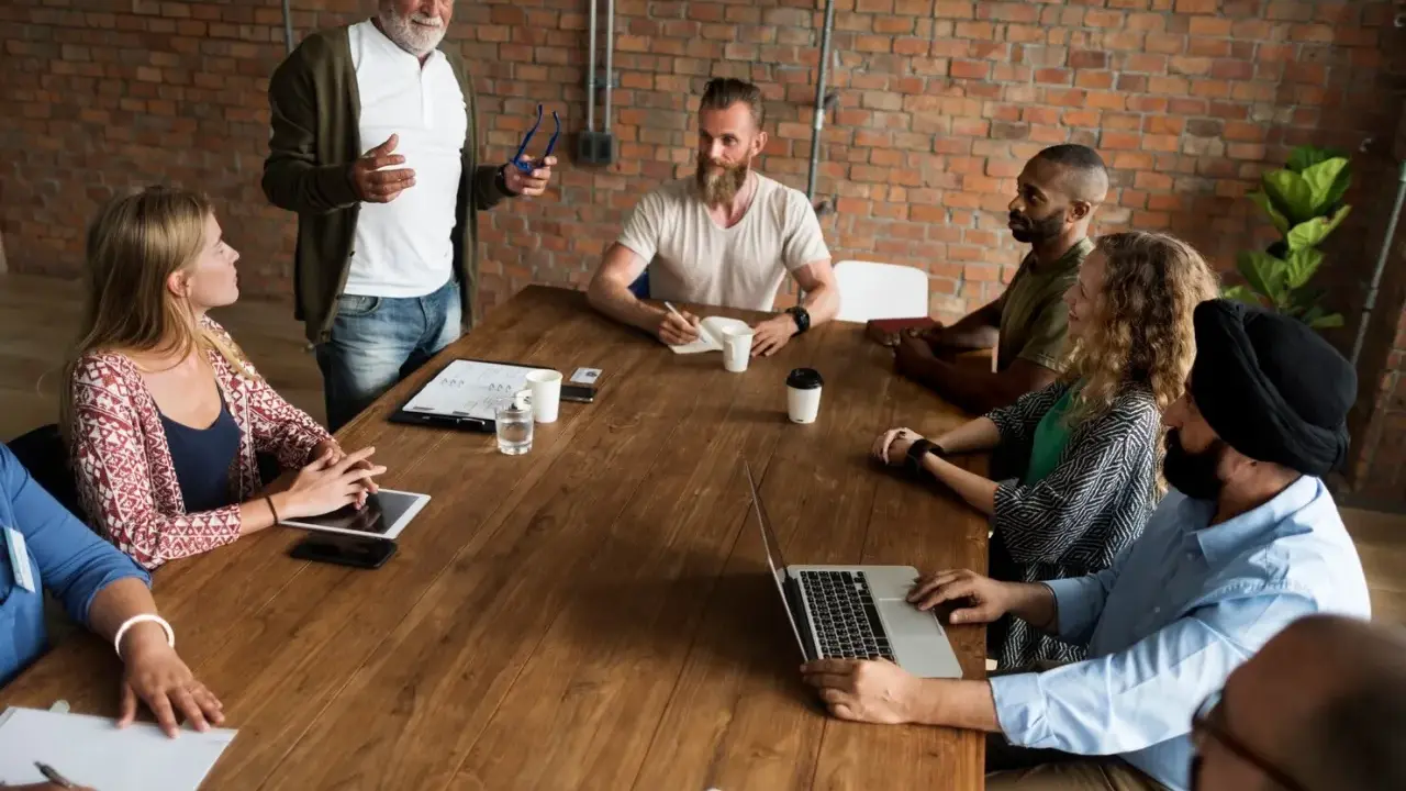 Un grupo diverso de personas participa en reuniones de empresa, discutiendo ideas alrededor de una mesa de madera.