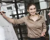 Mujer sonríe mientras explica un gráfico en un rotafolio, demostrando cómo liderar equipos con éxito.