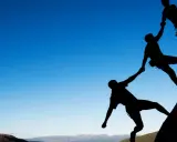 Siluetas de escaladores ayudándose mutuamente en una roca. Un ejemplo de cómo comportarse en el trabajo: colaboración y apoyo.