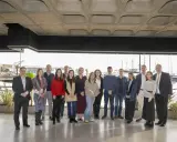 Grupo diverso posa para foto de graduación de un **advanced management program** frente a un puerto deportivo.