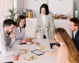 Equipo colaborando en una mesa con café y bocadillos. A pesar de las reuniones largas, el ambiente es positivo y productivo.
