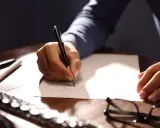 Mano escribiendo una carta formal con bolígrafo.