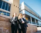 Tres jóvenes profesionales con trajes oscuros, con los brazos cruzados, posan frente a un edificio moderno. Aspiran a estar en los FT MBA rankings.