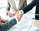 Apertón de manos entre hombres de negocios, con un contrato y gráficos sobre la mesa. Tácticas de negociación exitosas.