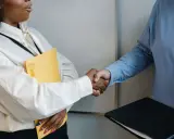 Dos personas se dan la mano, una con una carpeta amarilla, en un momento clave para negociar un salario.