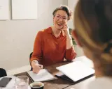 Mujer sonriente con gafas, tomando notas, discutiendo qué podrias aportar a la empresa.
