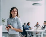 Mujer sonríe con tablet, en oficina moderna. Equipo discute estrategias de public management.