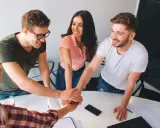 Equipo unido en formación de gestión de equipos. Jóvenes sonríen mientras juntan sus manos en señal de compromiso y colaboración.