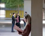 Estudiantes revisan materiales de estudio, como ejemplos de trabajos de oficina, en un campus universitario.
