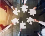Manos unidas colocando piezas de rompecabezas, un símbolo de inteligencia colaborativa y trabajo en equipo para lograr un objetivo común.