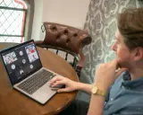 Hombre en videollamada con sus equipos virtuales. Varios rostros aparecen en la pantalla de su portátil, conectados desde diferentes lugares.