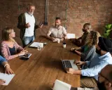 Un grupo diverso de personas participa en reuniones de empresa, discutiendo ideas alrededor de una mesa de madera.