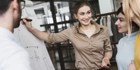 Mujer sonríe mientras explica un gráfico en un rotafolio, demostrando cómo liderar equipos con éxito.