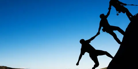 Siluetas de escaladores ayudándose mutuamente en una roca. Un ejemplo de cómo comportarse en el trabajo: colaboración y apoyo.
