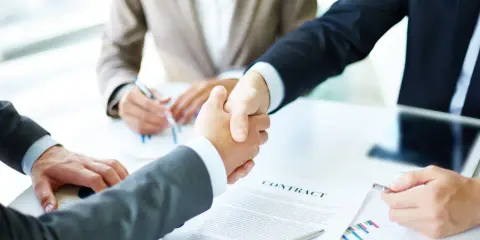 Apertón de manos entre hombres de negocios, con un contrato y gráficos sobre la mesa. Tácticas de negociación exitosas.