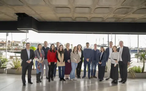 Grupo diverso posa para foto de graduación de un **advanced management program** frente a un puerto deportivo.