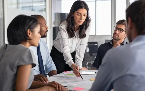 Mujeres y hombres en una reunión discutiendo un proyecto. La líder, con una blusa a cuadros, señala un documento, inspirando un **curso empoderamiento femenino**.