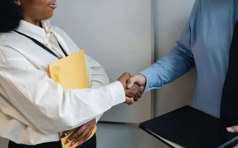 Dos personas se dan la mano, una con una carpeta amarilla, en un momento clave para negociar un salario.