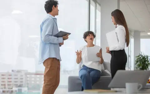 Tres colegas discuten un proyecto. La mujer sentada gesticula mientras explica, buscando cómo mejorar la comunicación interna de una empresa.