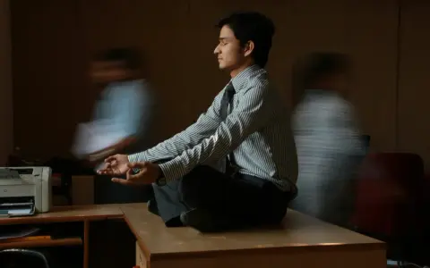 Un joven en posición de loto, con las manos en meditación, busca la calma en medio del ajetreo. Su serenidad contrasta con las figuras borrosas que lo rodean, reflejando la complejidad de la gestión sanitaria.