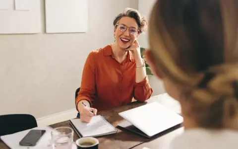Mujer sonriente con gafas, tomando notas, discutiendo qué podrias aportar a la empresa.