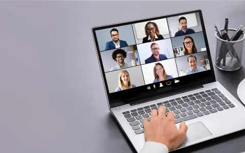 Persona interactúa con tecnología de videoconferencia, mostrando una cuadrícula de participantes en una reunión virtual.