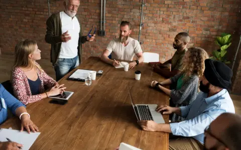 Un grupo diverso de personas participa en reuniones de empresa, discutiendo ideas alrededor de una mesa de madera.