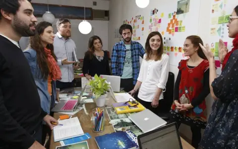 Equipo en una **stand up meeting** discutiendo ideas frente a un tablero lleno de notas adhesivas.
