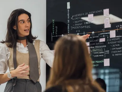 Mujer explica un diagrama en pizarra, parte de un programa de desarrollo de gestión.