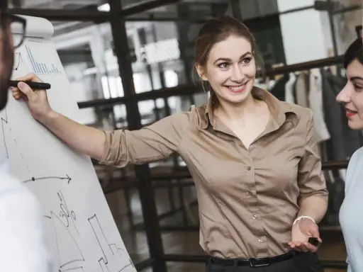 Mujer sonríe mientras explica un gráfico en un rotafolio, demostrando cómo liderar equipos con éxito.