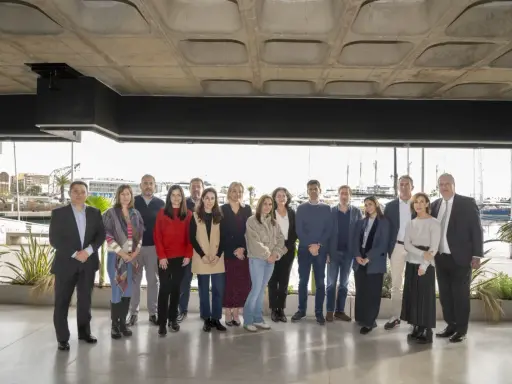 Grupo diverso posa para foto de graduación de un **advanced management program** frente a un puerto deportivo.