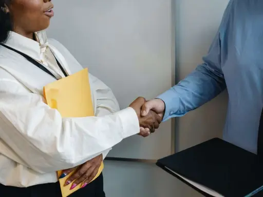 Dos personas se dan la mano, una con una carpeta amarilla, en un momento clave para negociar un salario.