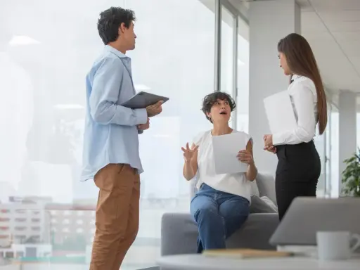 Tres colegas discuten un proyecto. La mujer sentada gesticula mientras explica, buscando cómo mejorar la comunicación interna de una empresa.