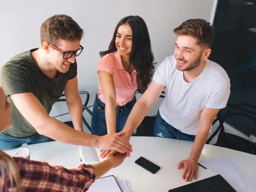 Equipo unido en formación de gestión de equipos. Jóvenes sonríen mientras juntan sus manos en señal de compromiso y colaboración.