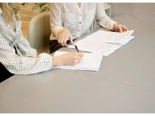 Dos mujeres revisan documentos en una mesa. Una escribe notas, un paso clave en cómo ser un CEO.