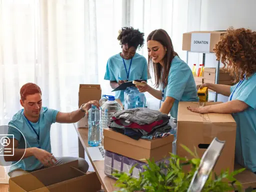 Voluntarios organizan donaciones. Un hombre revisa una lista, mientras otros empaquetan ropa y agua. Su cv volunteering es valioso.