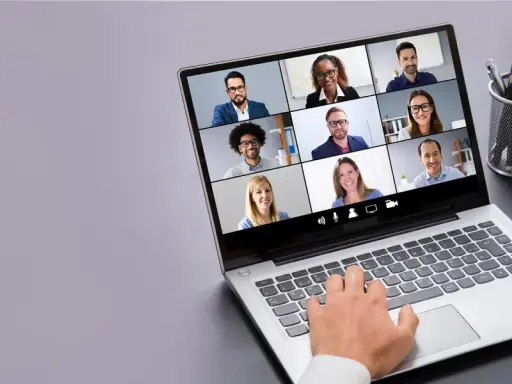 Persona interactúa con tecnología de videoconferencia, mostrando una cuadrícula de participantes en una reunión virtual.