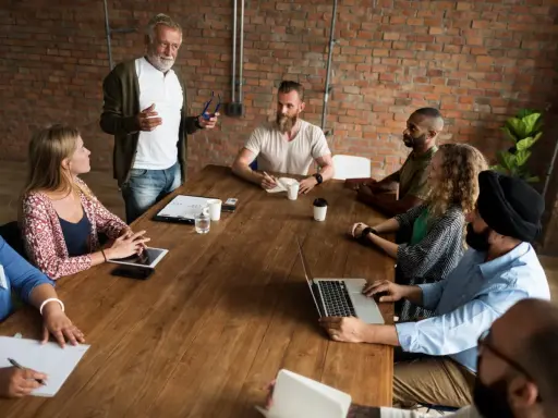 Un grupo diverso de personas participa en reuniones de empresa, discutiendo ideas alrededor de una mesa de madera.