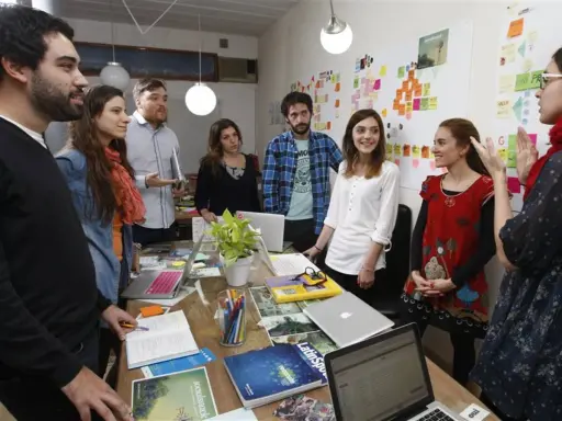 Equipo en una **stand up meeting** discutiendo ideas frente a un tablero lleno de notas adhesivas.