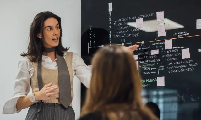 Mujer explica un diagrama en pizarra, parte de un programa de desarrollo de gestión.