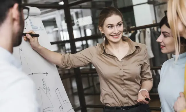 Mujer sonríe mientras explica un gráfico en un rotafolio, demostrando cómo liderar equipos con éxito.